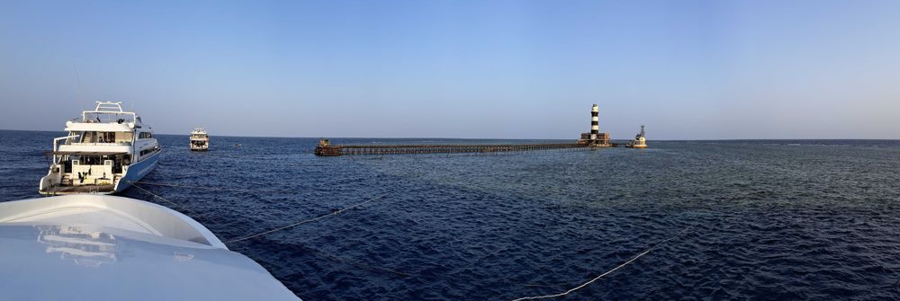 Des bateaux amarrés au pied d'un phare, sur un récif au large, accesible qu'en crosière.