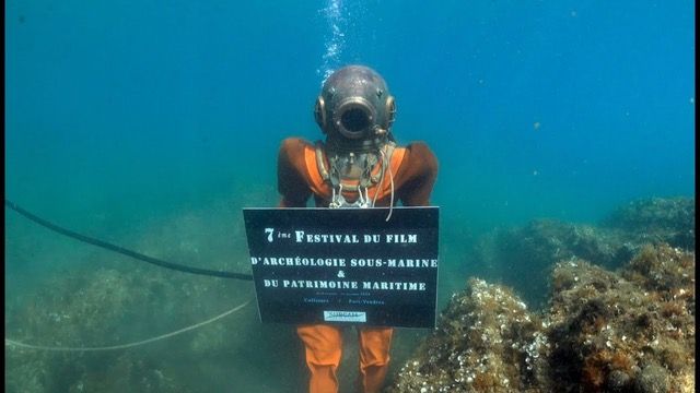 Un scaphandrier avec un panneau autour du cou, indiquant "7ème édition du festival"